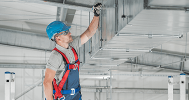 Man in a hard hat inspecting HVAC vents.